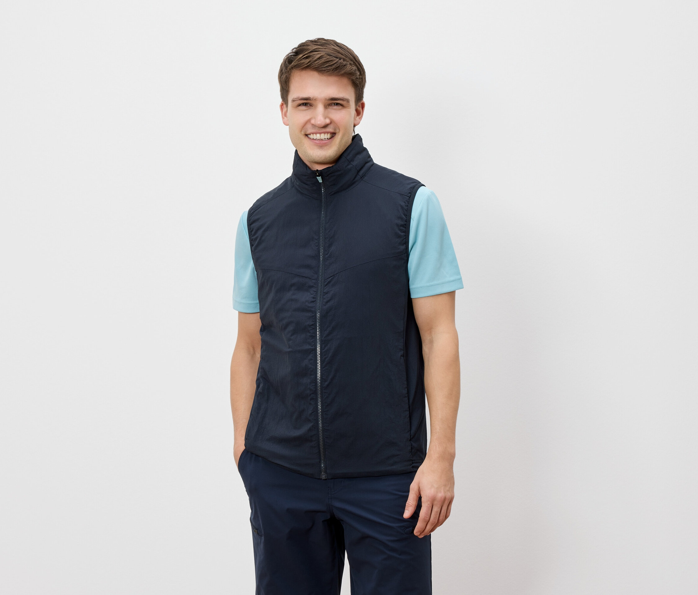 Mężczyzna uśmiecha się do kamery, ubrany w granatową kamizelkę na jasnoniebieską koszulkę.