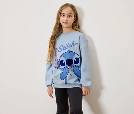 Dziewczyna z długimi blond włosami ma na sobie jasnoniebieską bluzę z nadrukiem Stitch i czarne legginsy.