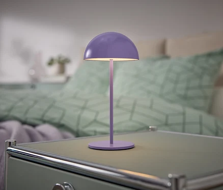 Fioletowa lampka stoi na szafce nocnej obok łóżka.