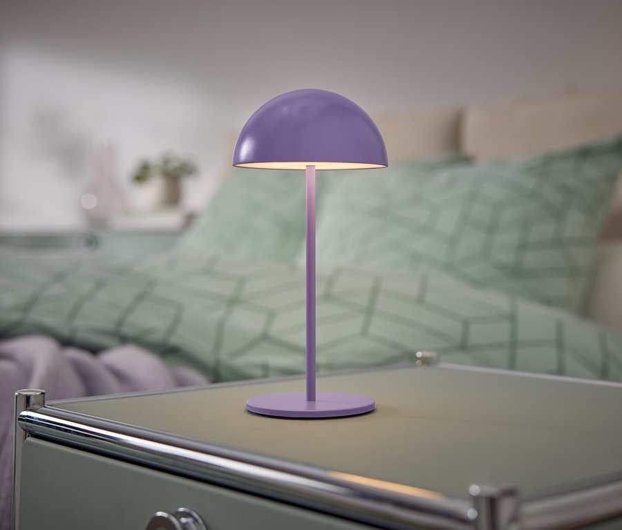 Fioletowa lampka stoi na szafce nocnej obok łóżka.