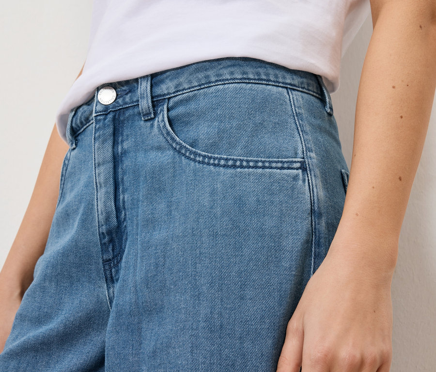 Zbliżenie kobiety w jasnoniebieskich dżinsach i białej koszulce.