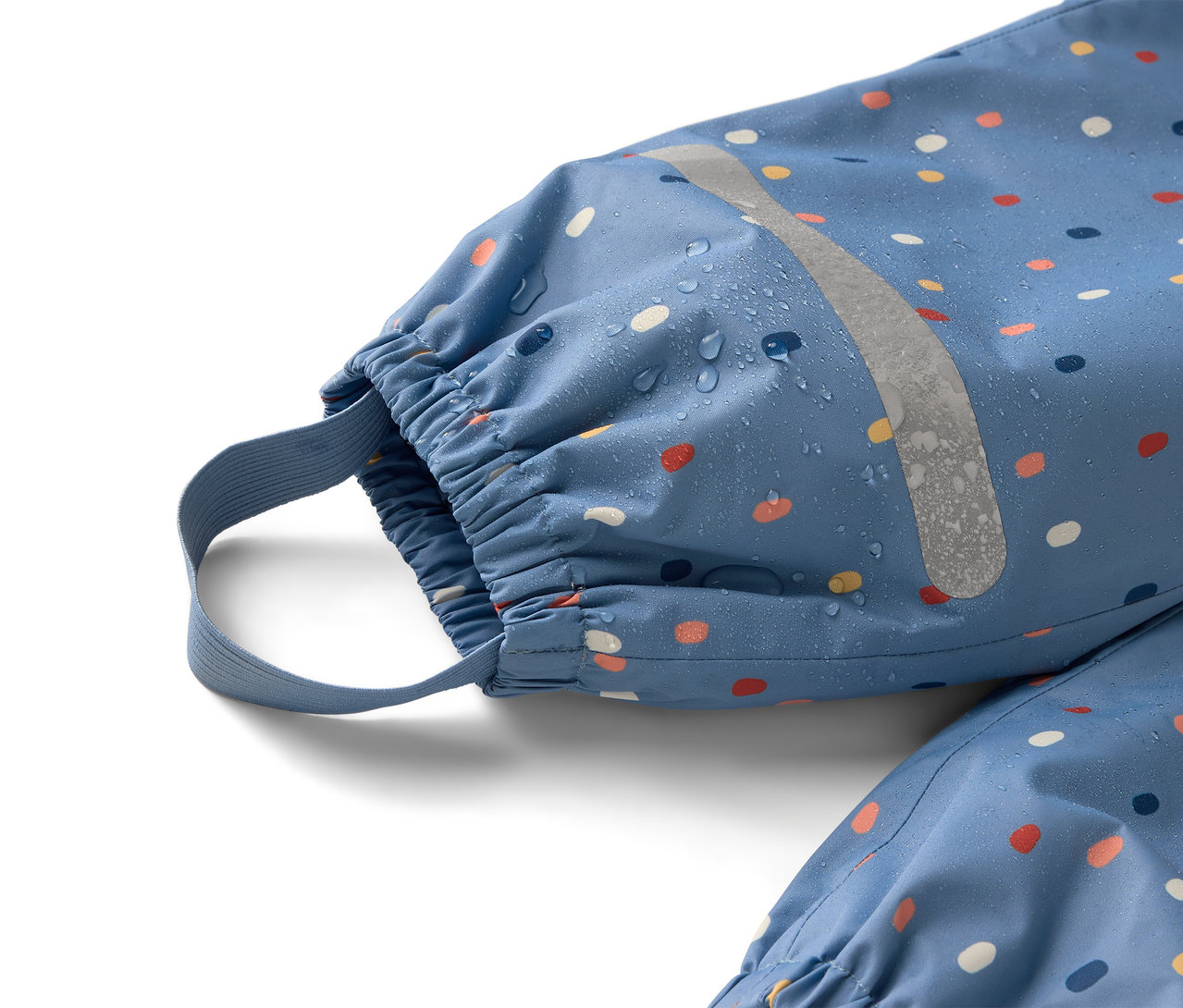 Zbliżenie na niebieski kombinezon przeciwdeszczowy w kolorowe kropki z odblaskowym paskiem, na którym widać krople wody.