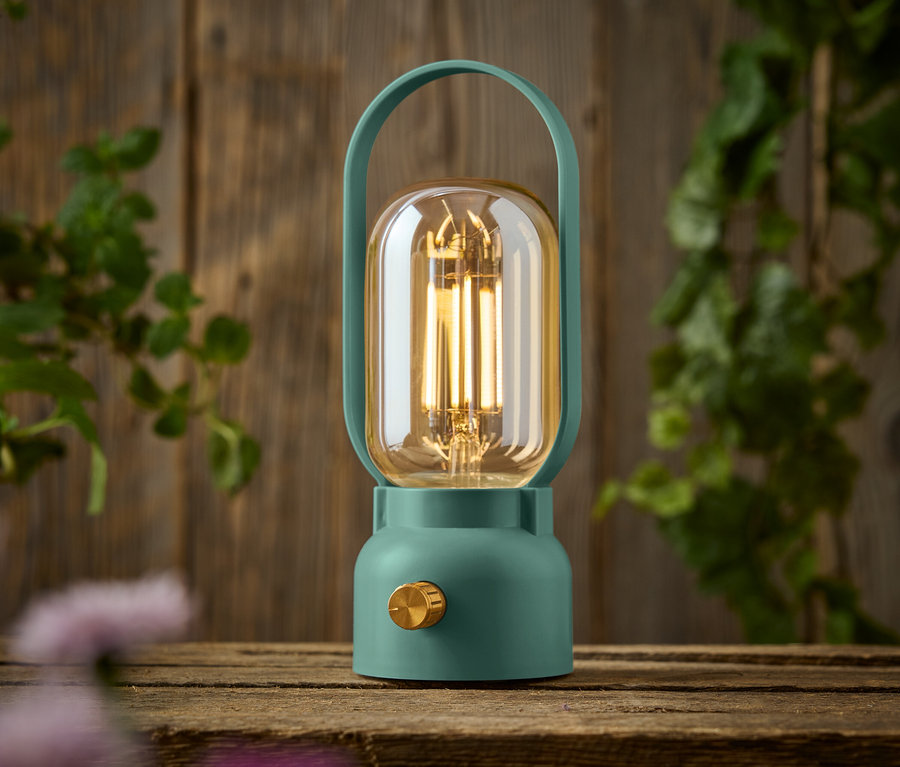 Zielona lampa z złotym pokrętłem stoi na drewnianym stole.