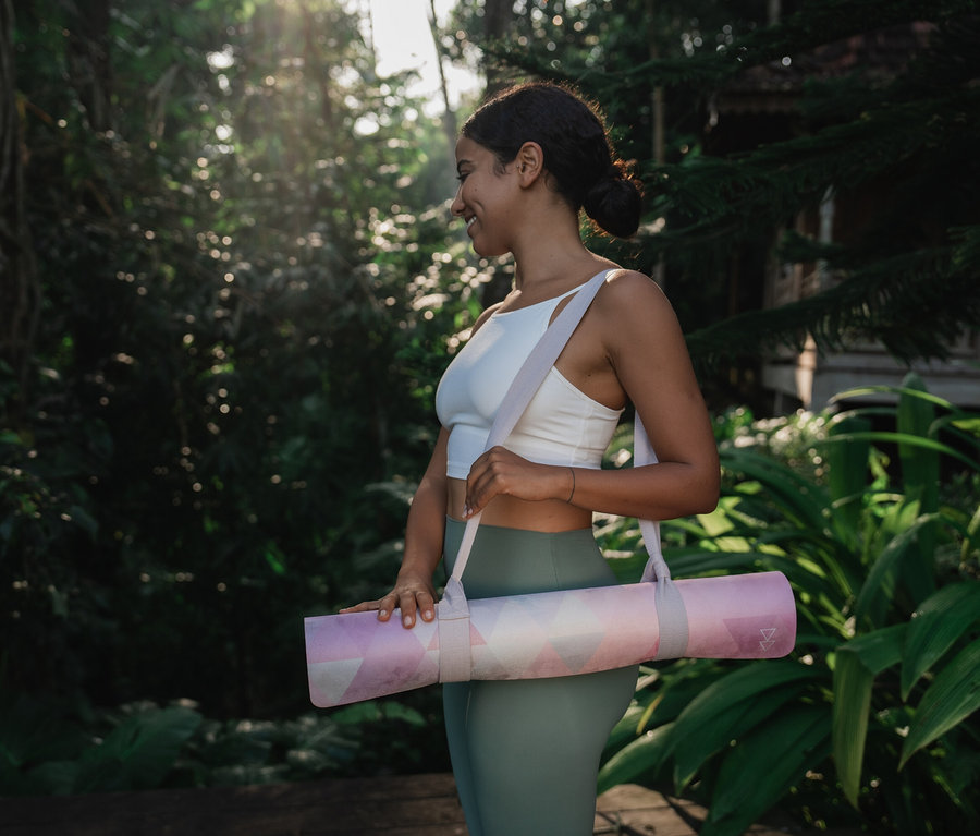 Kobieta niesie zwiniętą matę do jogi na łonie natury.