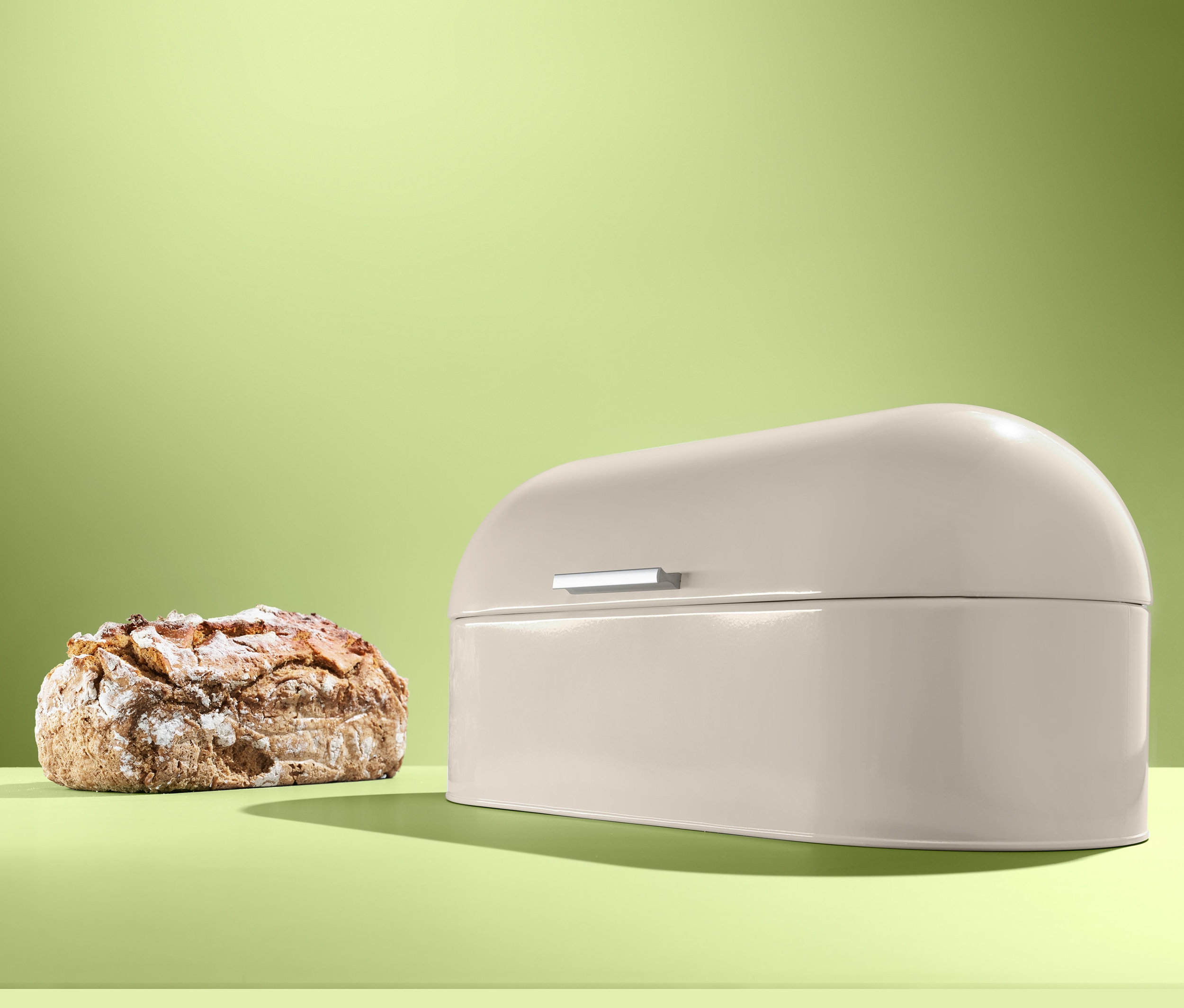 Bochenek chleba obok beżowego metalowego chlebaka.