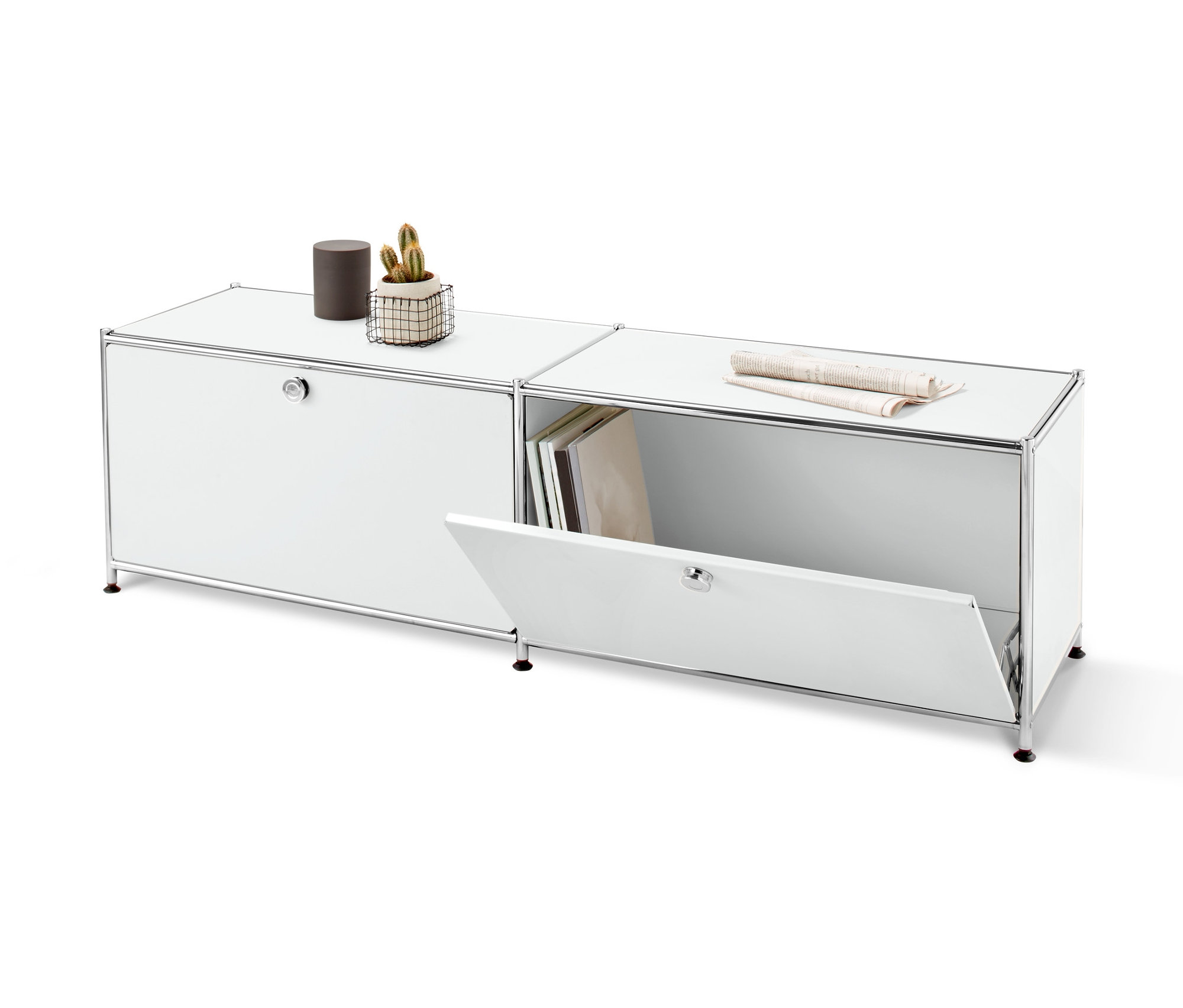 Dwie białe metalowe szafki typu lowboard z klapami. Na jednej szafce stoi brązowa puszka i kaktus w koszyku, druga ma otwartą klapę i leży na niej gazeta.