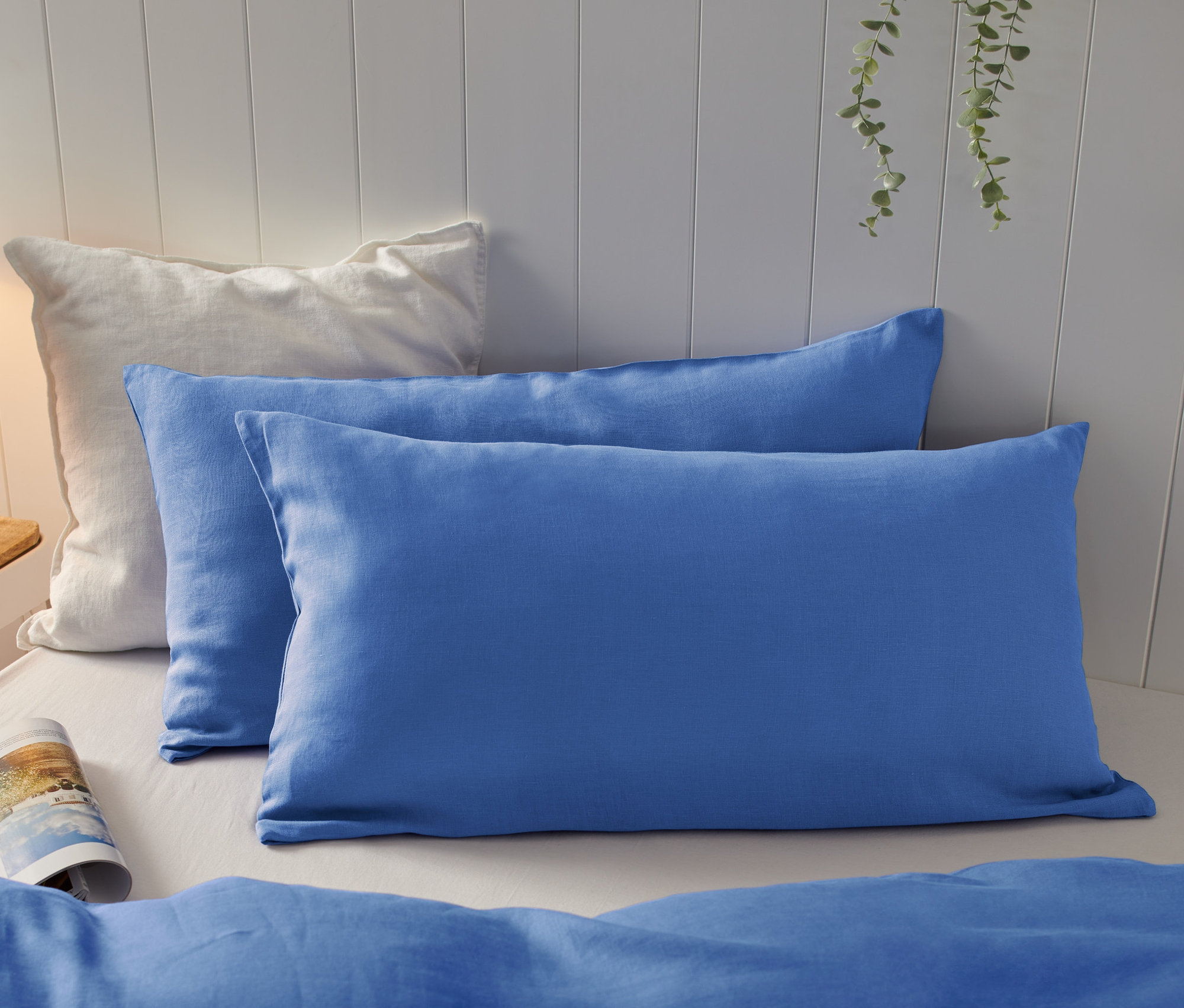 Na łóżku leżą dwie poszewki na poduszki z lnu o wymiarach 80 x 40 cm, jedna biała i jedna niebieska.