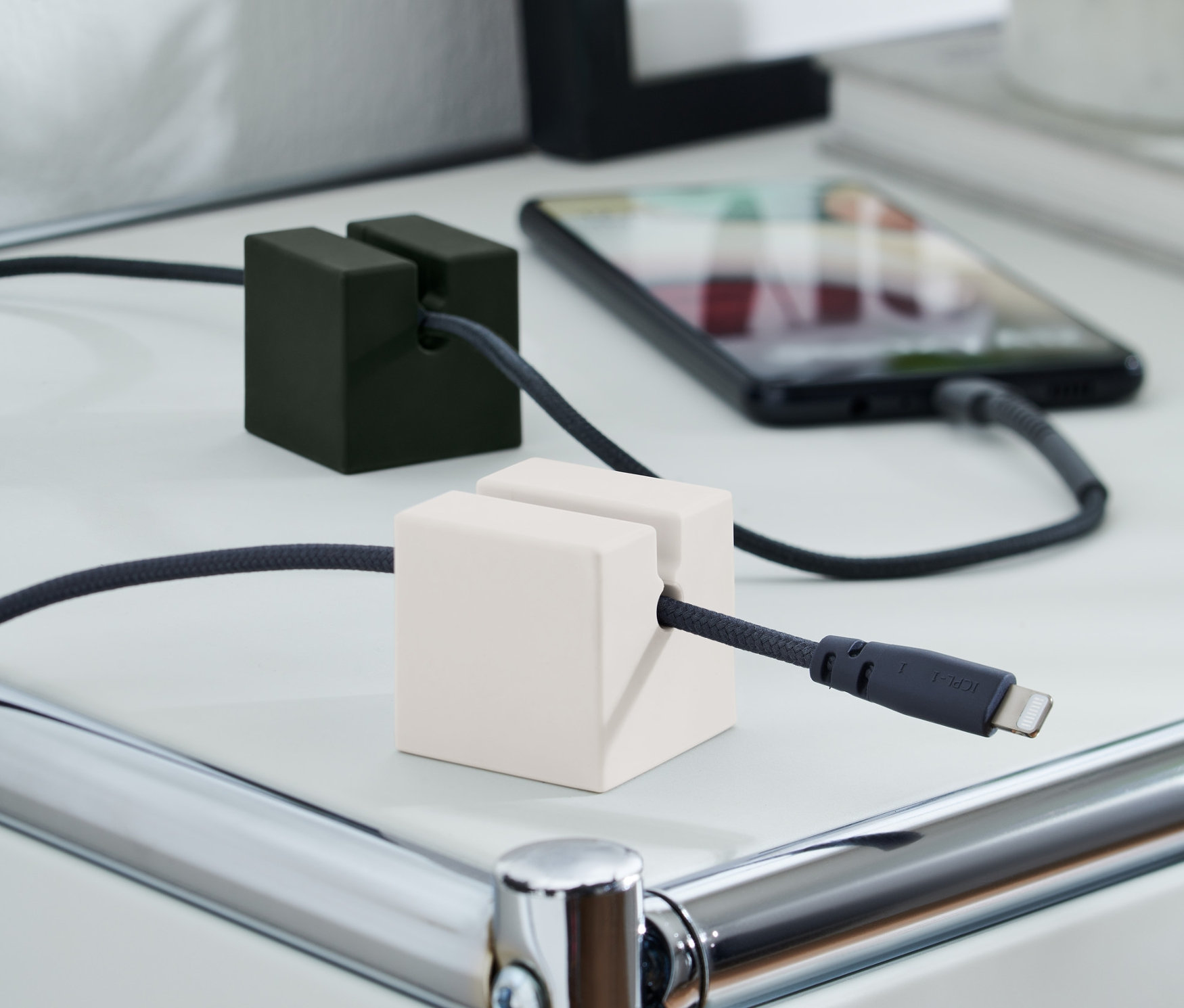 Dwa organizery na przewód do ładowania, 2 sztuki w zestawie, trzymają przewody do ładowania na białym stole. Jeden jest czarny, a drugi biały.