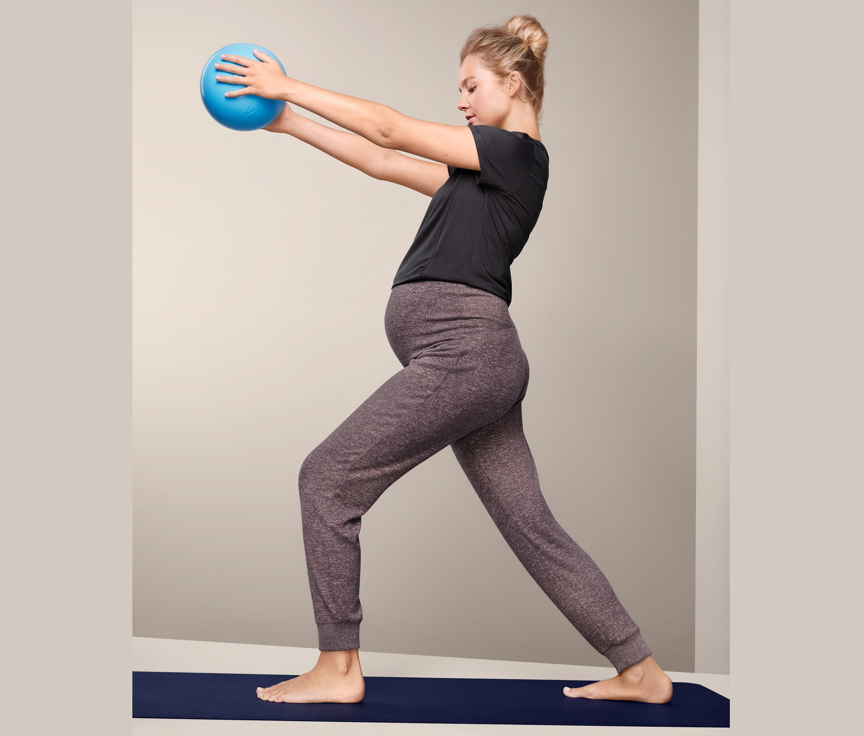 Kobieta w ciąży ćwiczy z niebieską piłką na macie i ma na sobie Rekreacyjne spodnie ciążowe.