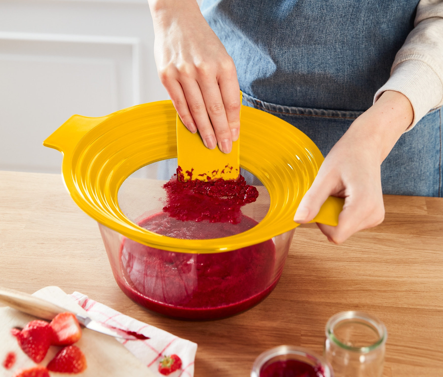 Kobieta przeciera czerwone puree przez żółte sitko do przesiewania mąki i przecierania 2 w 1.