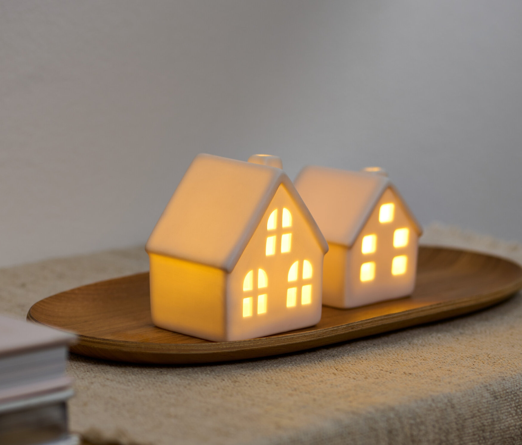Dwa ceramiczne domki LED na drewnianej tacy.