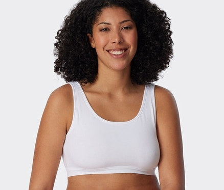 Kobieta ma na sobie biały biustonosz braletkę z bawełny ekologicznej SCHIESSER z 2-częściowego zestawu i białe majtki.