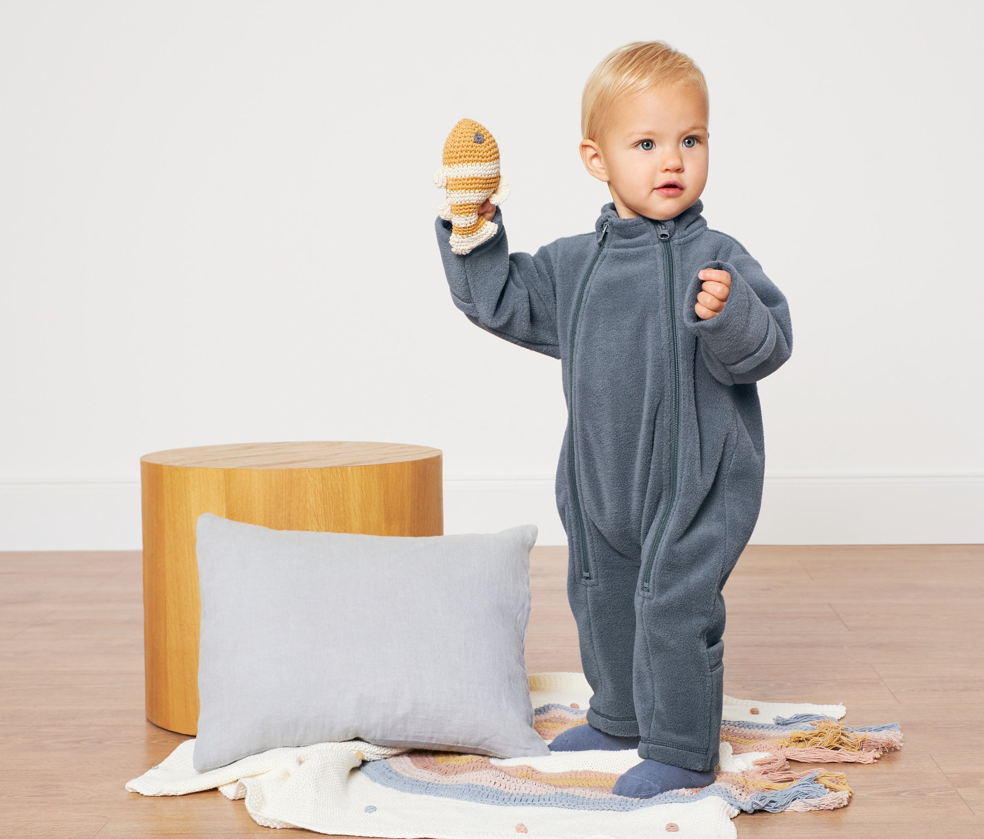 Maluch w niebieskim kombinezonie z polaru trzyma zabawkę rybę.