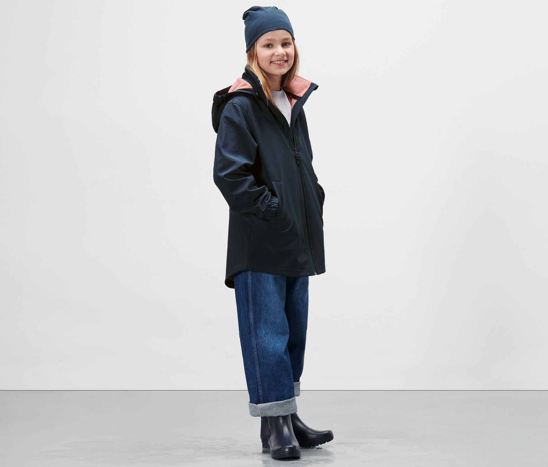 Dziewczyna ma na sobie granatowy płaszcz z softshellu, dżinsy i czapkę.