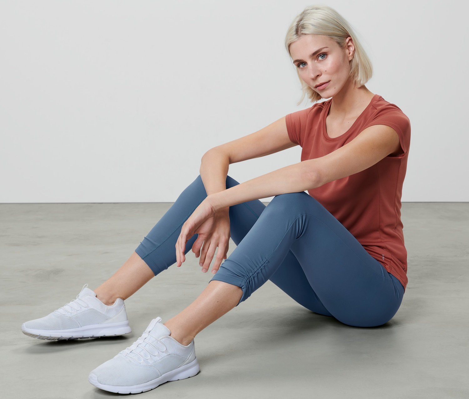 Kobieta siedzi na podłodze w legginsach sportowych 7/8 i koszulce.
