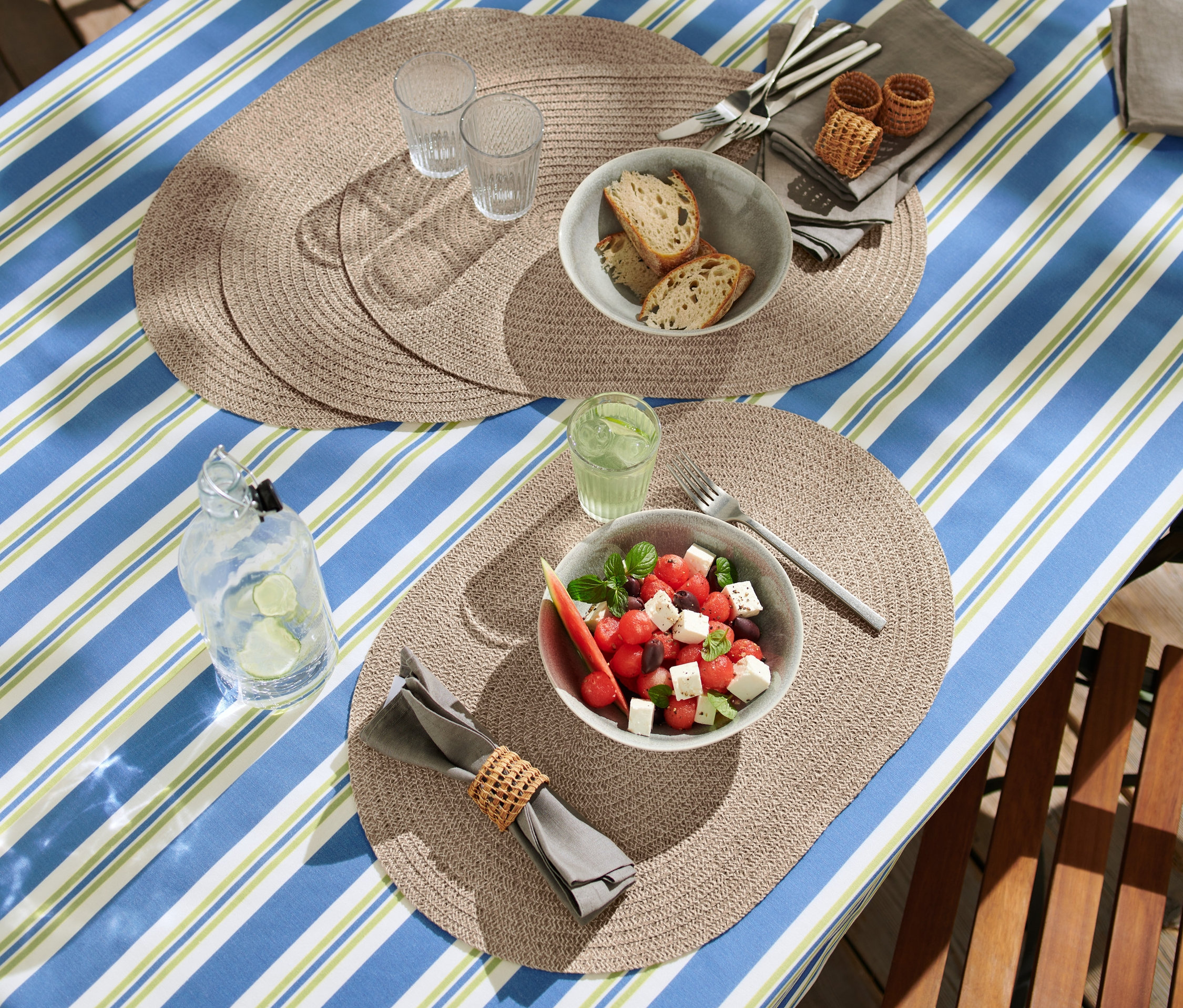 Nakryty stół z zmywalnymi podkładkami na stół (4 sztuki), sałatką z arbuza, chlebem i napojami.