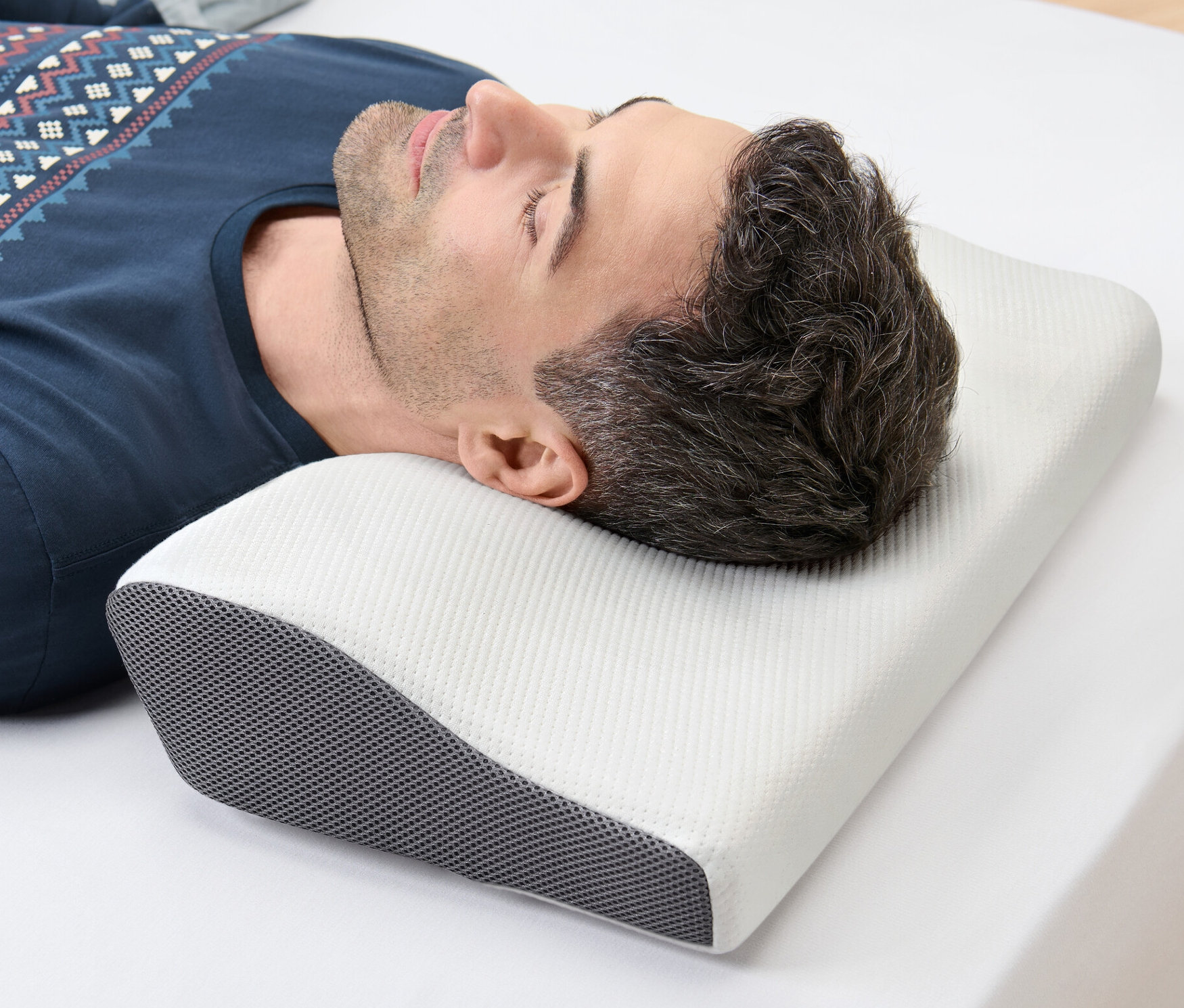 Mężczyzna leży na boku na białym prześcieradle z głową na poduszce pod kręgi szyjne.