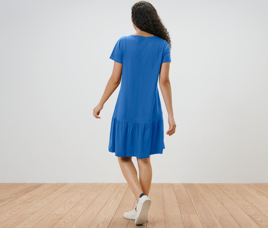 Kobieta w kobaltowej sukience dżersejowej z falbaną, widziana z tyłu.