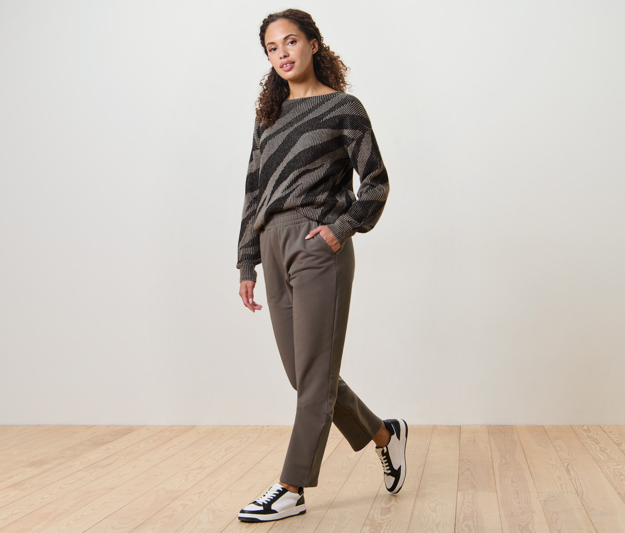 Kobieta idzie, ubrana w spodnie joggery i wzorzysty sweter.