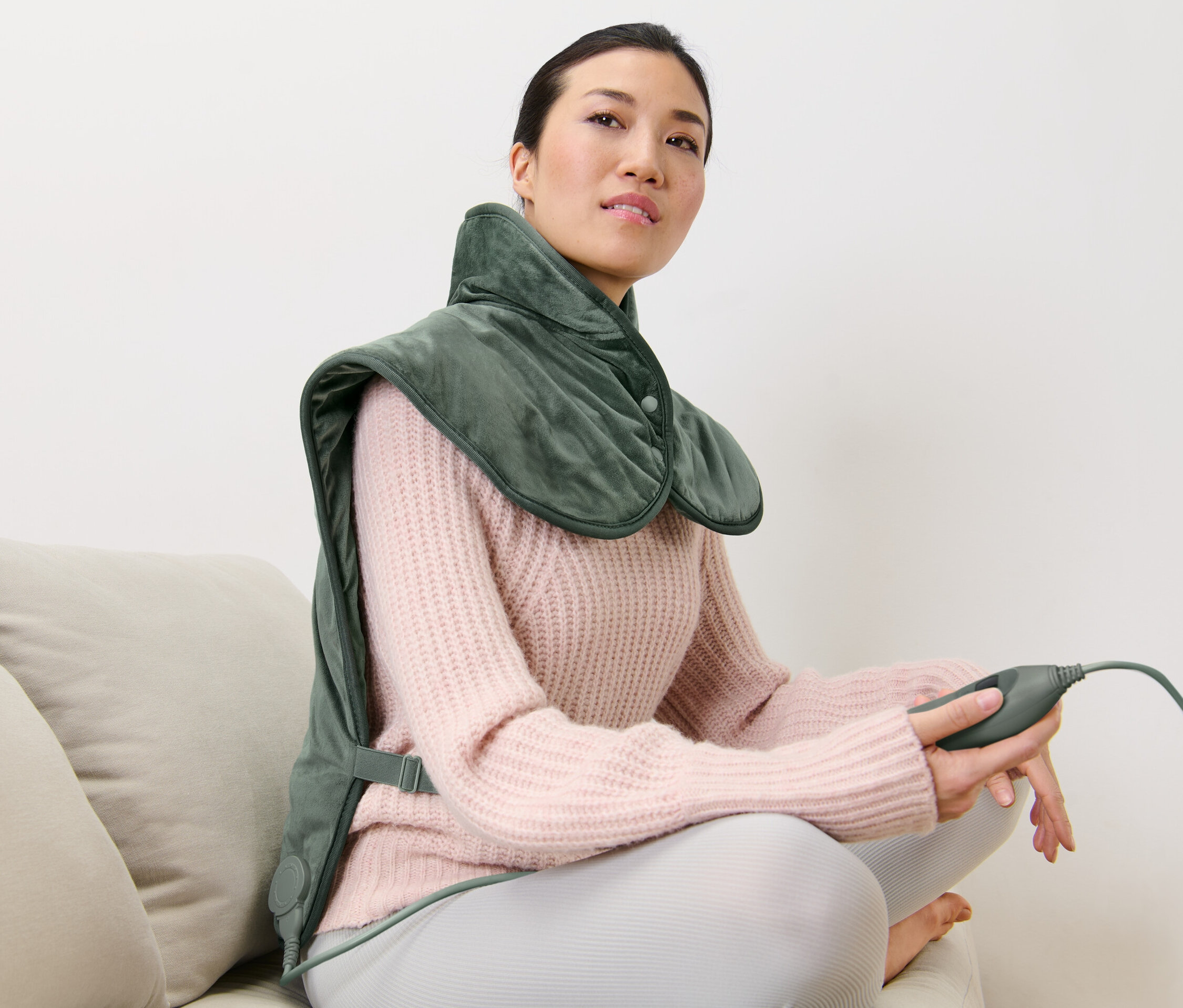 Kobieta siedzi na kanapie i ma na sobie poduszkę elektryczną na plecy.