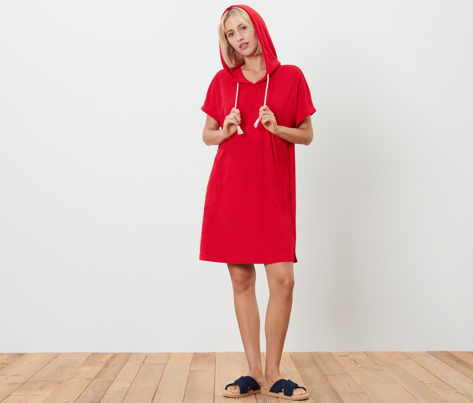Blondwłosa kobieta pozuje w czerwonej sukience plażowej z tkaniny frotte z kapturem i sznurkiem.