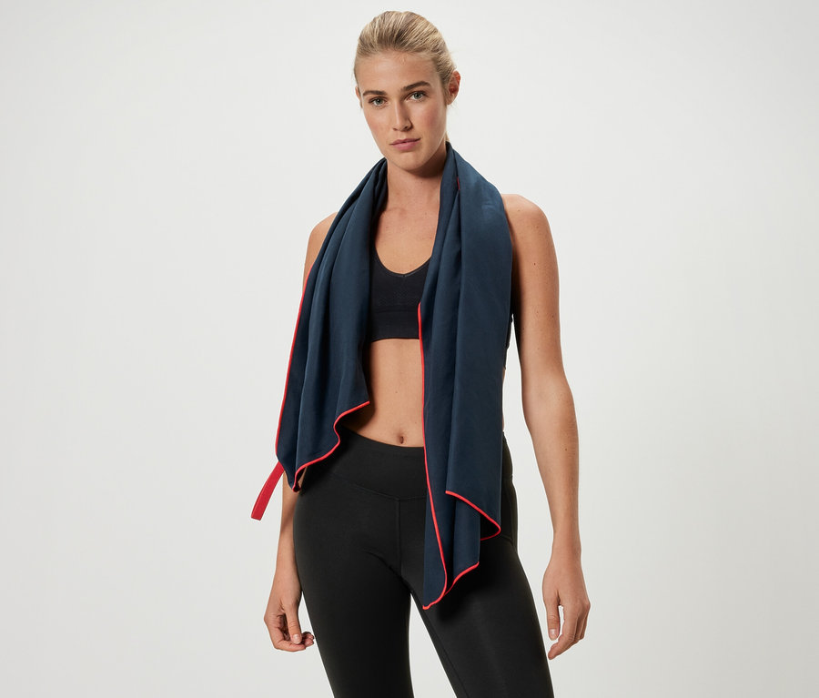 Blondwłosa kobieta ma na szyi ręcznik sportowy z czerwoną obwódką.