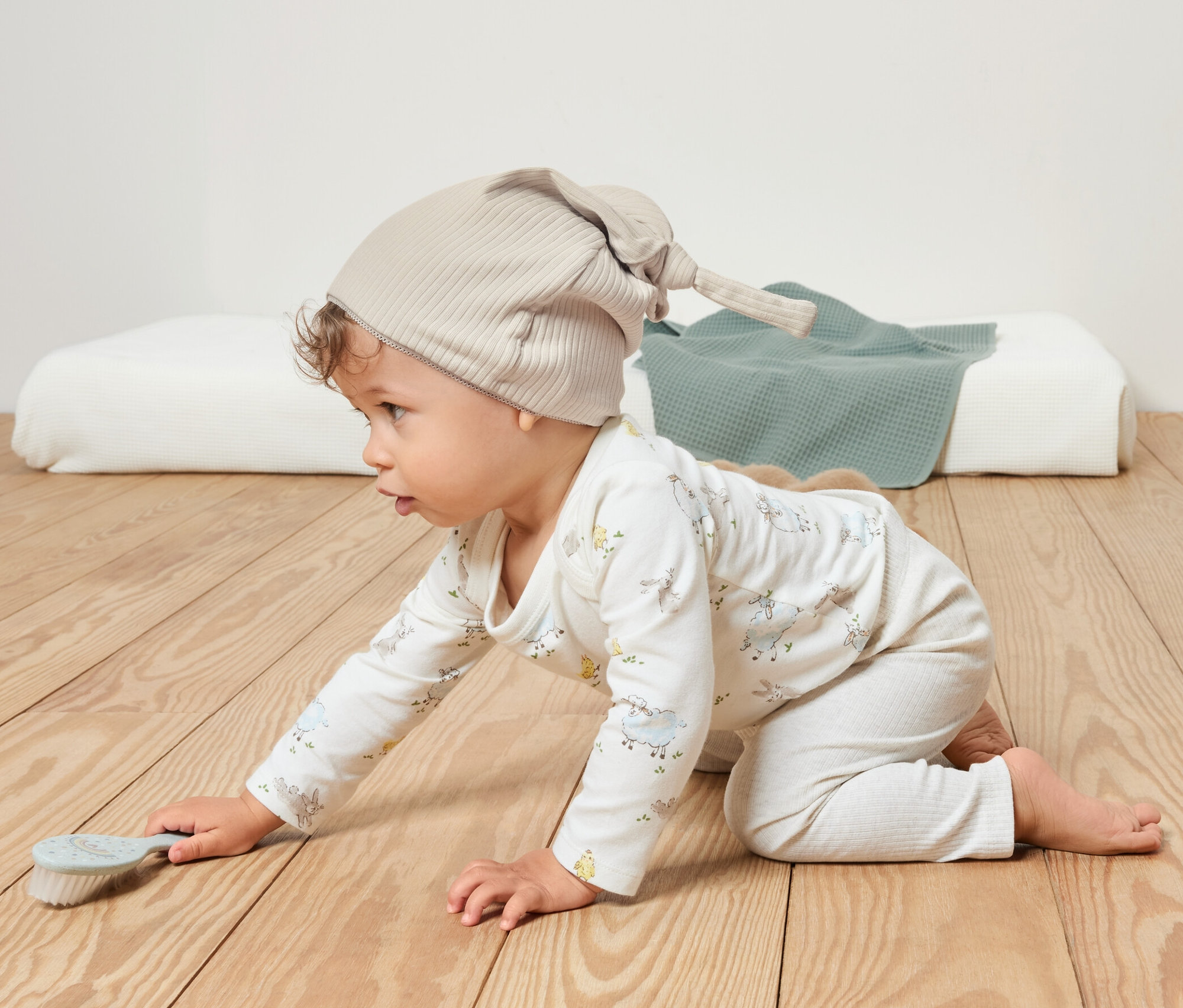 Dziecko raczkuje po drewnianej podłodze, ma na sobie beżową czapkę z dżerseju.