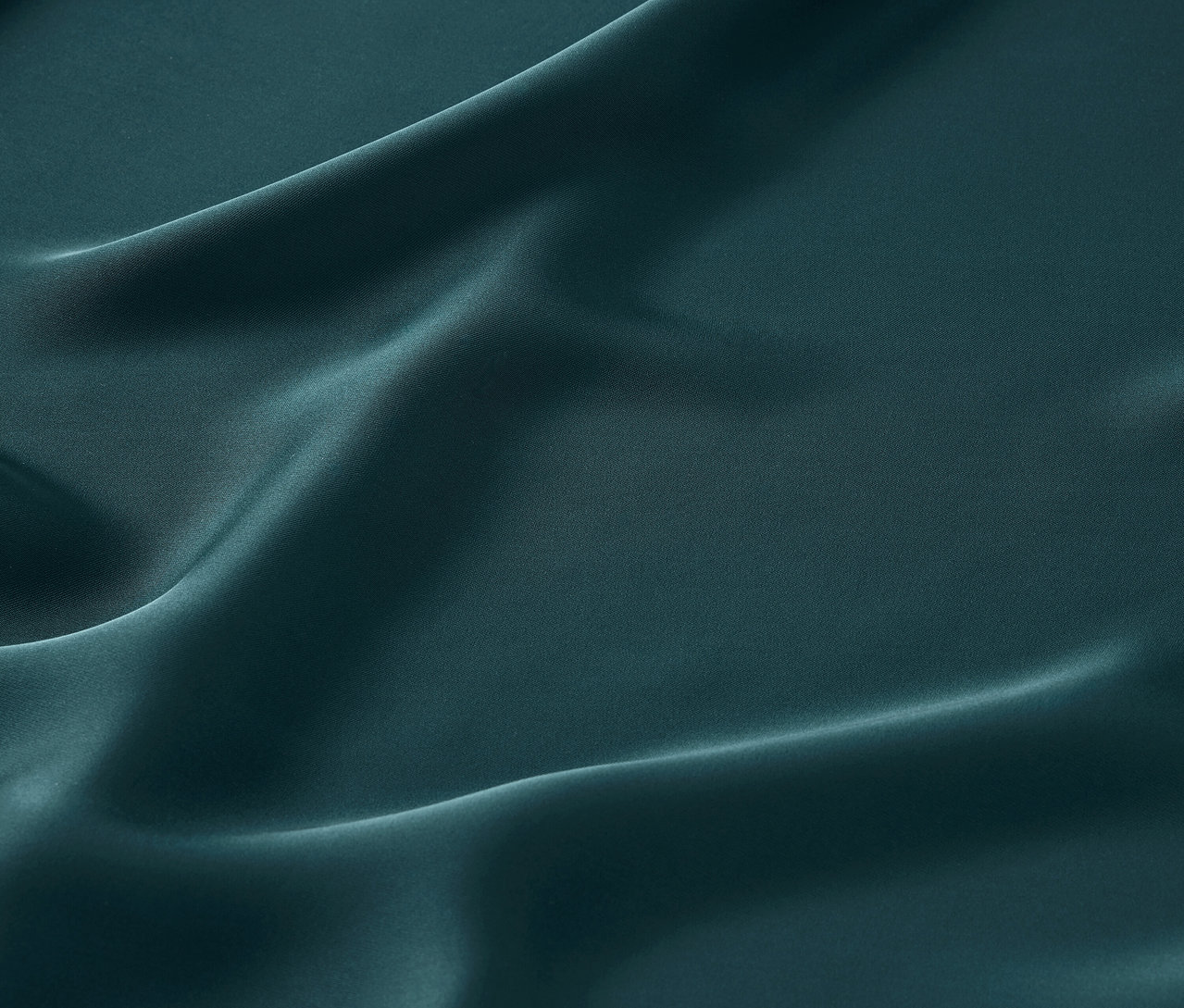 Zbliżenie na szmaragdowozieloną satynową tkaninę z delikatnymi fałdami.