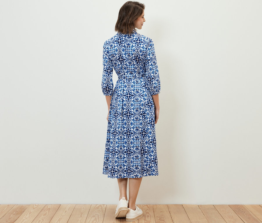 Kobieta stoi tyłem do aparatu i ma na sobie sukienkę midi z nadrukiem.