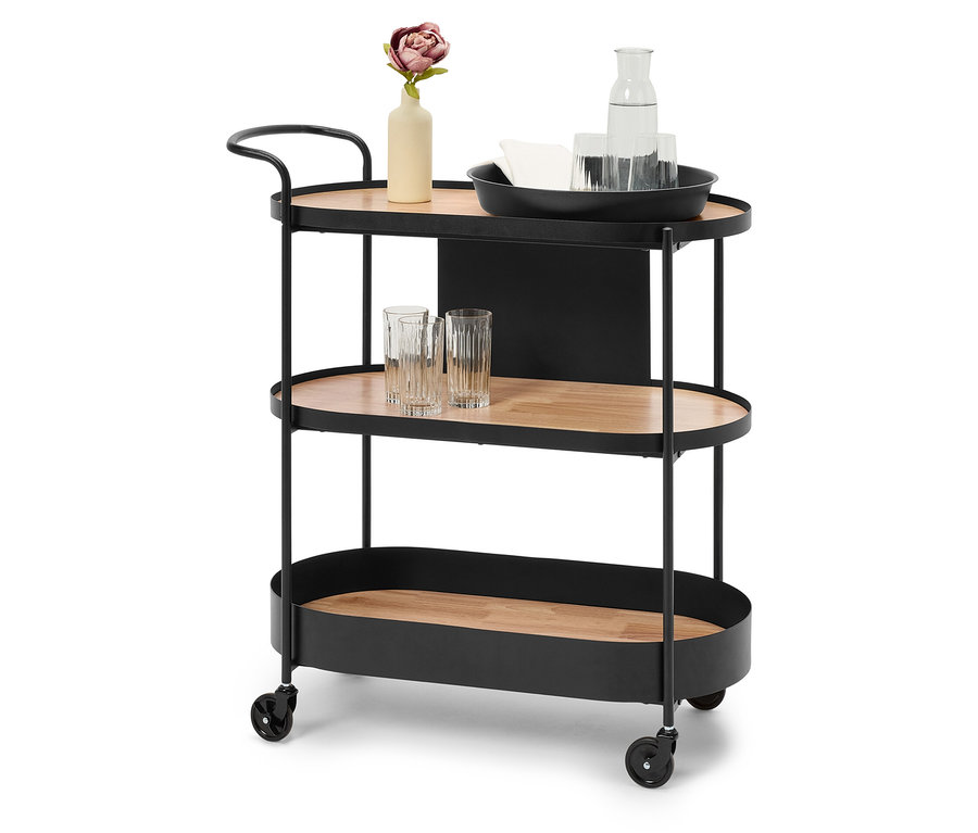 Czarny wózek barowy z trzema półkami z brązowego drewna, na górnej półce wazon z kwiatem, karafka z wodą i szklanki.
