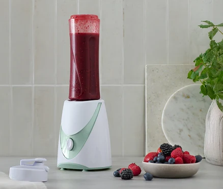 Mini-Smoothie-Maker z gotowym koktajlem na wierzchu, obok miska z jagodami.