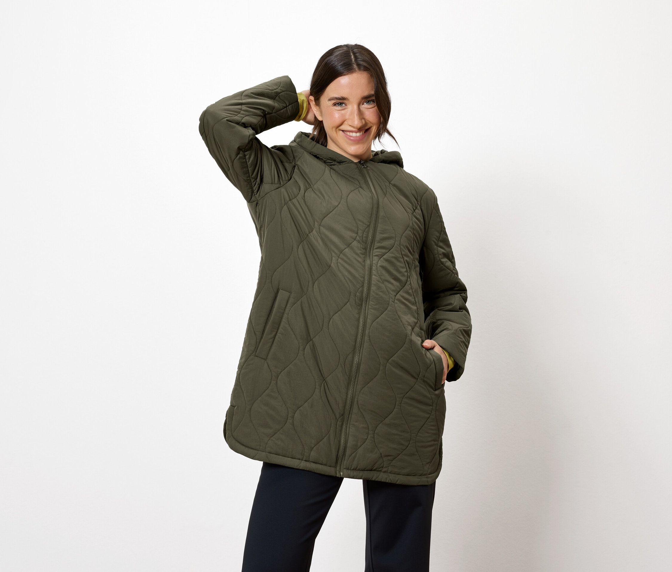Kobieta pozuje w oliwkowozielonej kurtce z kapturem i granatowych spodniach.