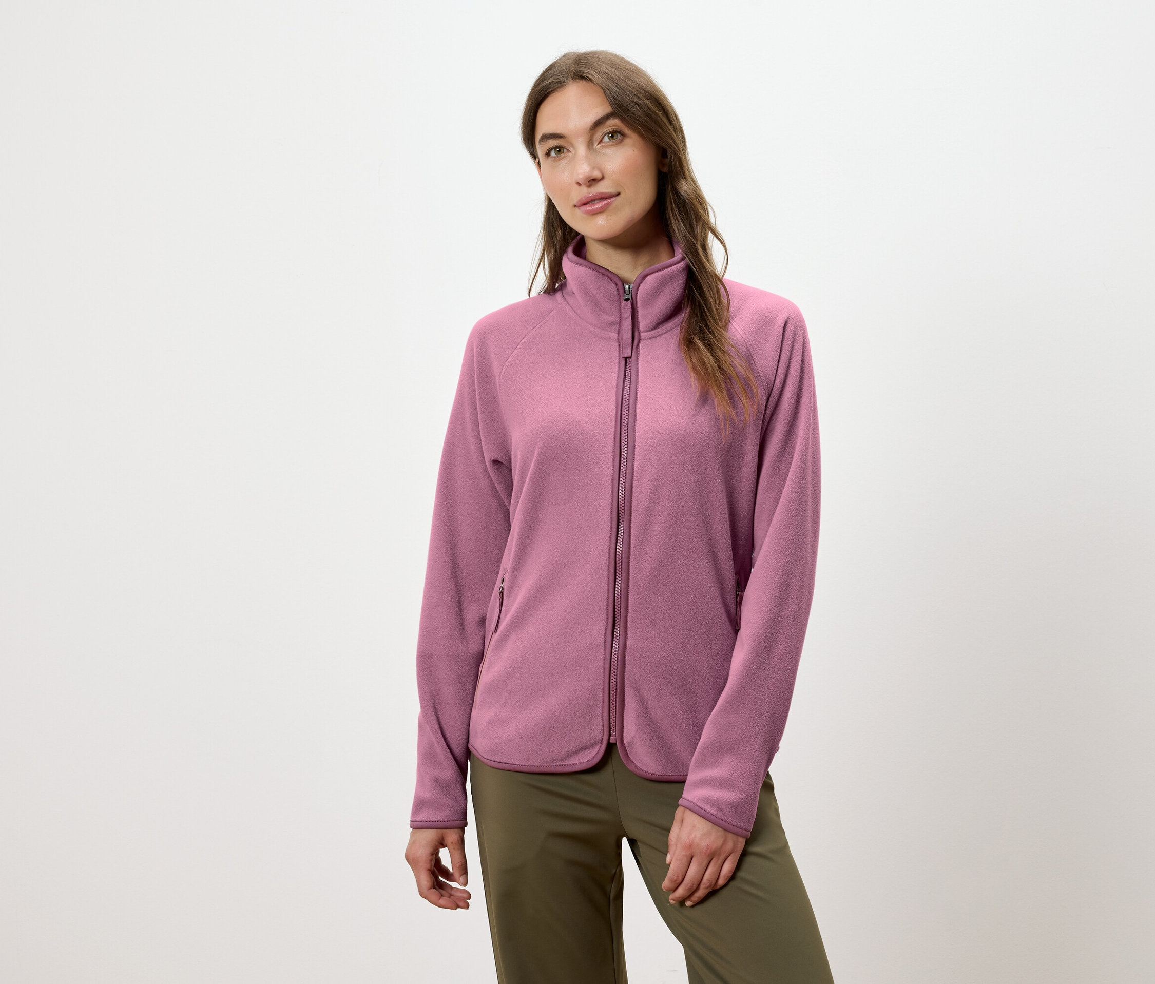 Kobieta ma na sobie różową bluzę polarową zapinaną na zamek i zielone spodnie.