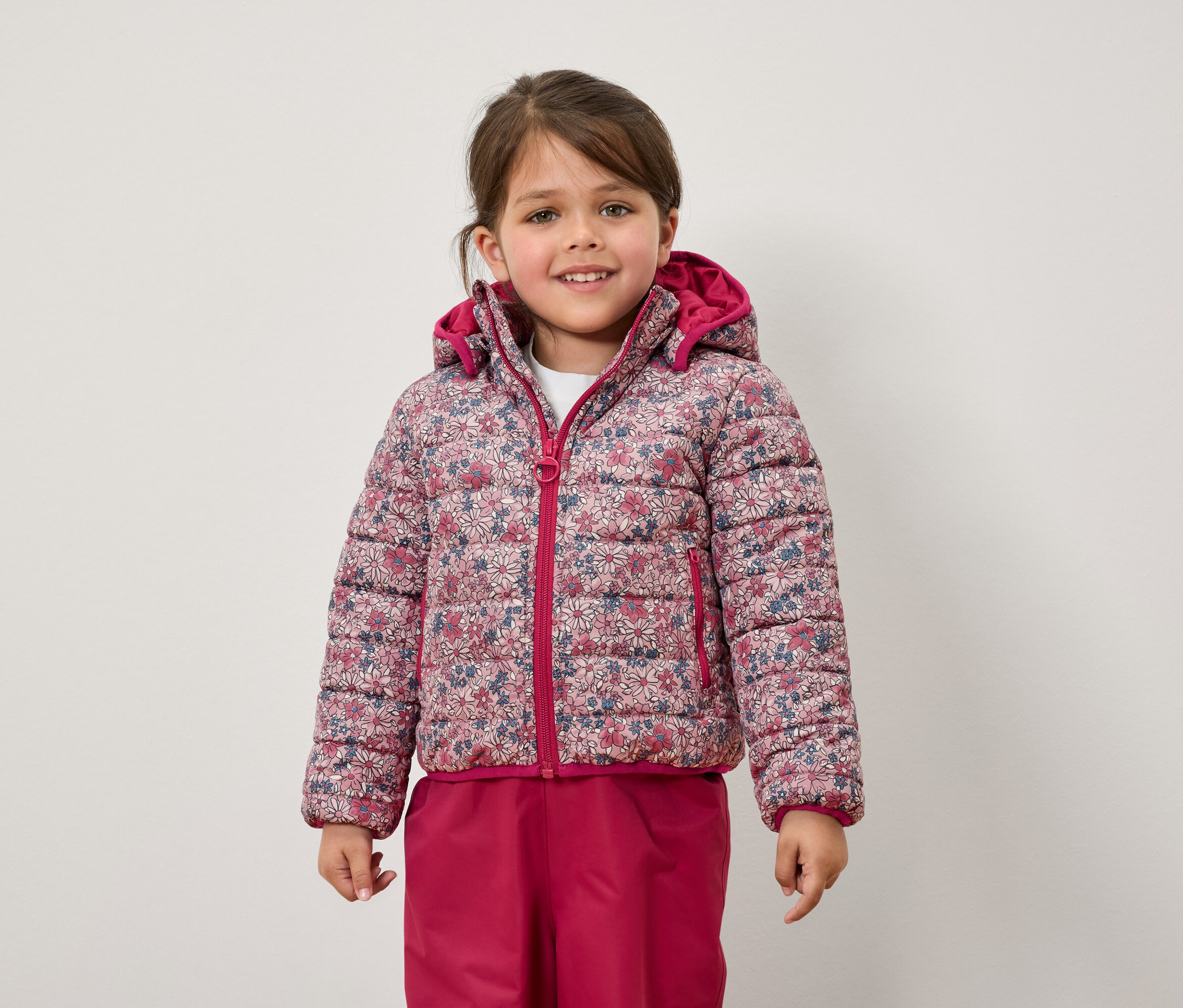 Dziewczynka ma na sobie kurtkę w kwiaty i różowe spodnie.
