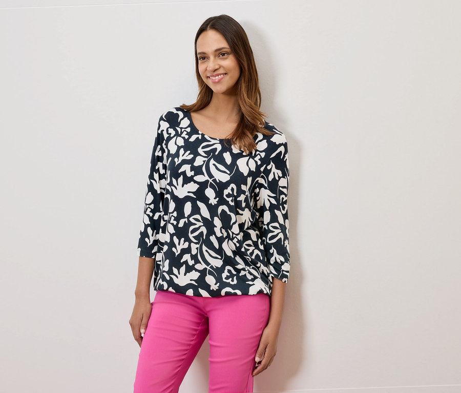 Kobieta ma na sobie granatową bluzkę w kwiaty i różowe spodnie.