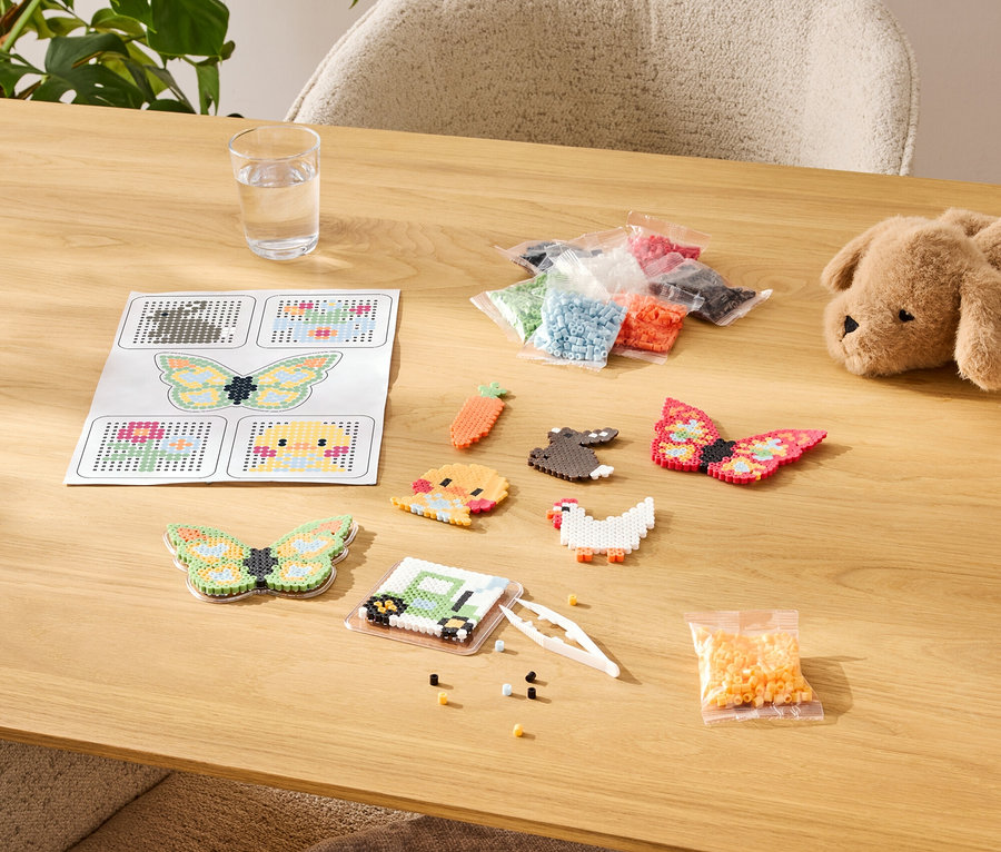 Stół z zestawem do tworzenia z koralików do prasowania, w tym szablony, gotowe wzory i asortyment kolorów w torebkach.