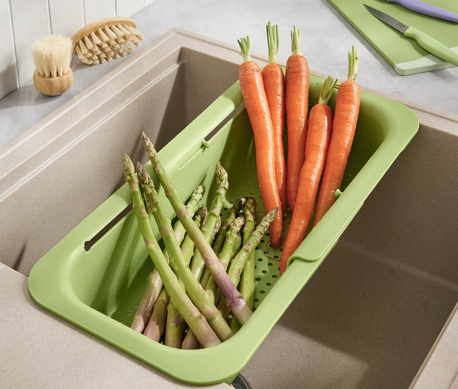 Marchewki i szparagi leżą w zielonym ociekaczu w zlewie.
