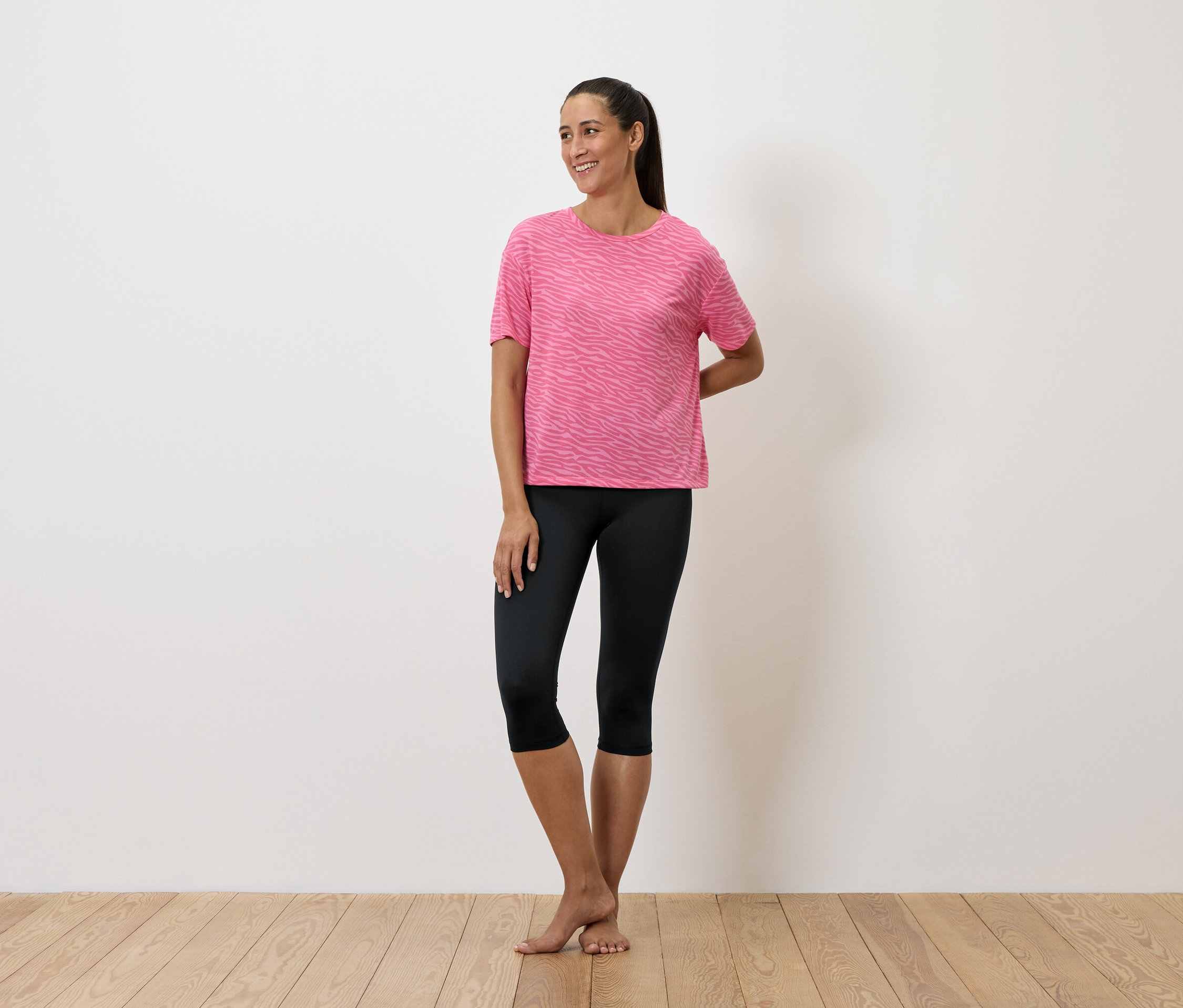 Kobieta stoi w różowej koszulce i czarnych legginsach.