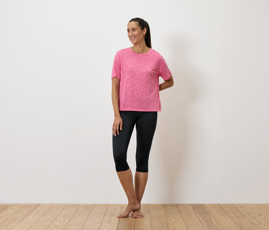 Kobieta stoi w różowej koszulce i czarnych legginsach.