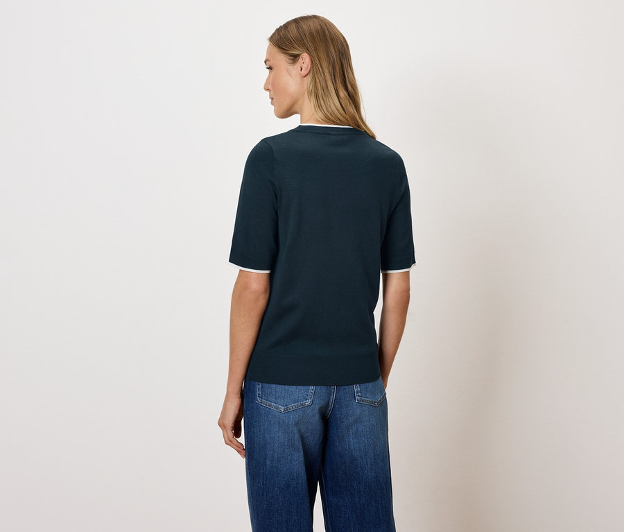 Kobieta pozuje tyłem do aparatu w granatowym topie i dżinsach.