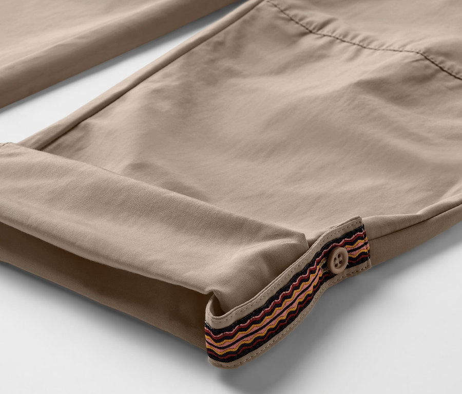 Szczegół beżowych spodni outdoorowych z podwiniętymi nogawkami i ozdobnym obszyciem z guzikiem. Spodnie mają ochronę przed komarami.