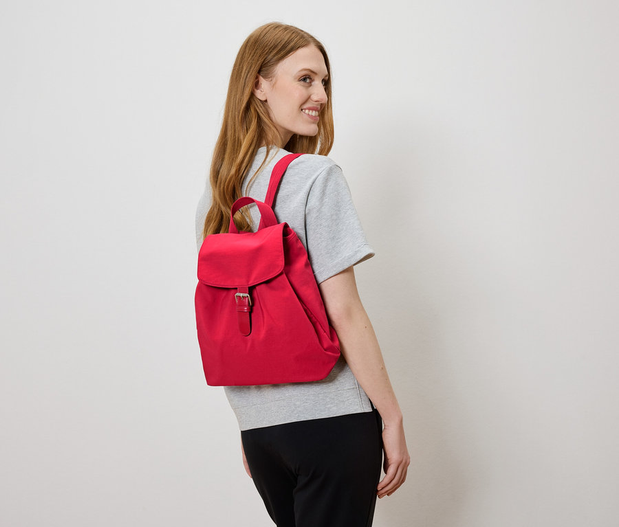 Kobieta z czerwonym plecakiem na plecach, patrzy w lewo.