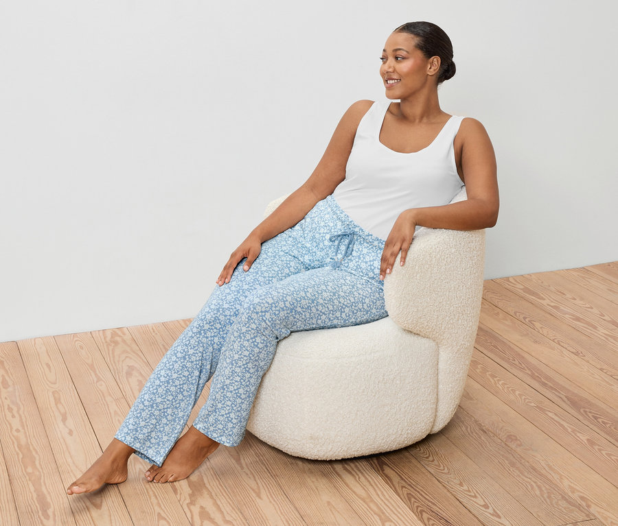 Kobieta siedzi w fotelu, ubrana w białą koszulkę i niebieskie spodnie.