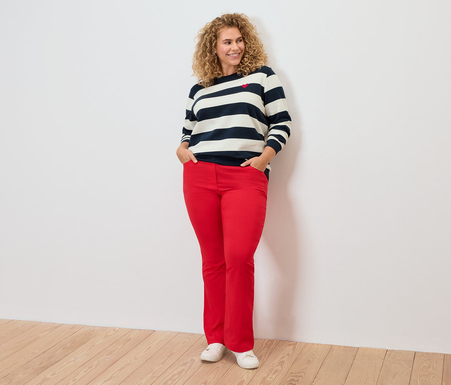 Kobieta z kręconymi włosami ma na sobie bluzkę w paski i czerwone spodnie.