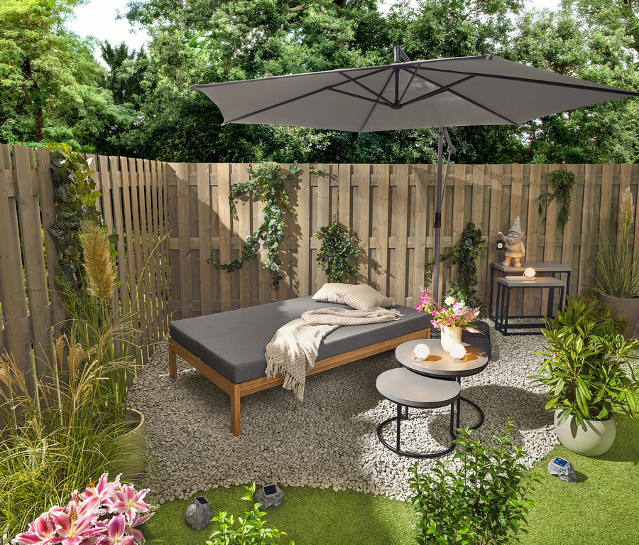 Ławka ogrodowa 2 w 1, która służy jako podwójny leżak, stoi obok dwóch stolików ogrodowych z blatami z polikrymentu (ok. 50 cm i 60 cm średnicy). Krasnal ogrodowy z latarnią LED stoi na jednym z 2 stolików konsolowych z blatami z polikrymentu. Widoczne są również trzy lampki stołowe z akumulatorem i trzy solarne kamienie LED.