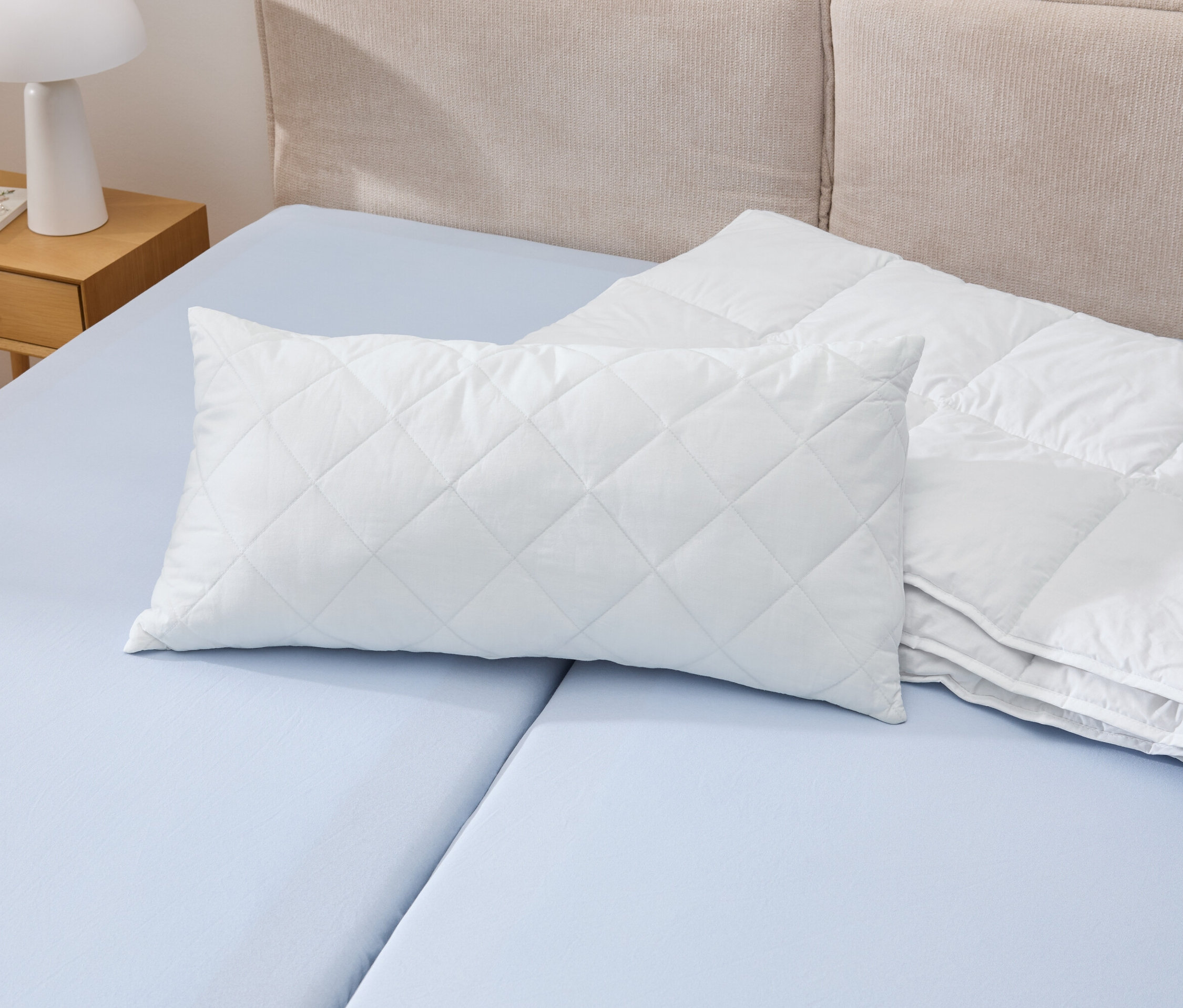 Biała poduszka Cell Solution® o wymiarach 80 x 40 cm leży na niebieskim łóżku obok białej kołdry.
