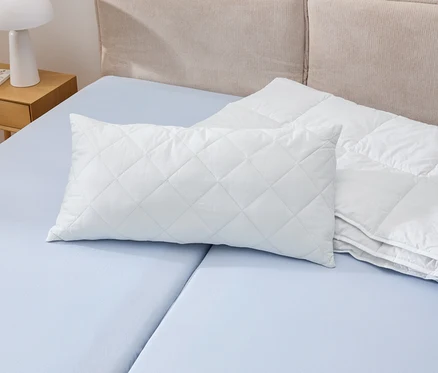 Biała poduszka Cell Solution® o wymiarach 80 x 40 cm leży na niebieskim łóżku obok białej kołdry.