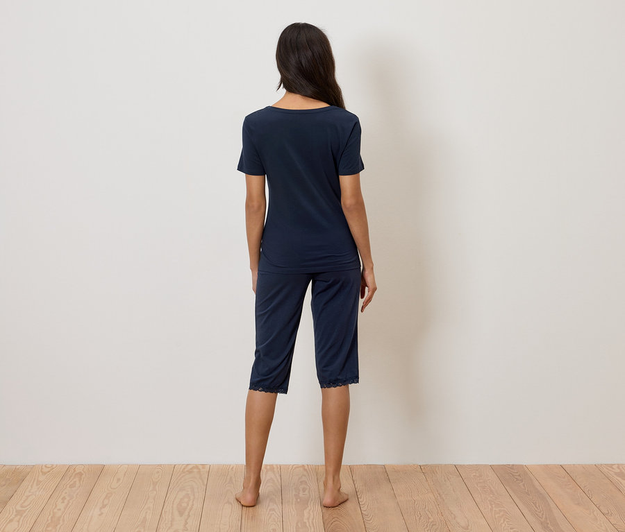 Kobieta stoi tyłem do kamery, ubrana w granatową piżamę z koronkowym wykończeniem.