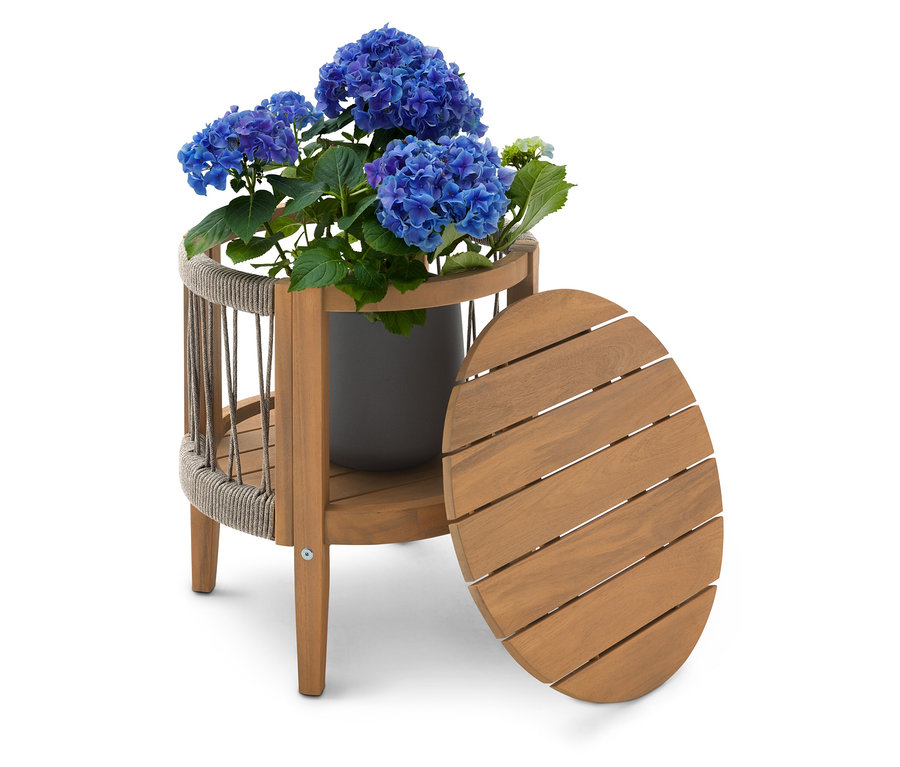 Niebieski krzew hortensji w szarej doniczce na dwupoziomowym drewnianym stoliku bocznym z owalnym blatem stojącym obok.
