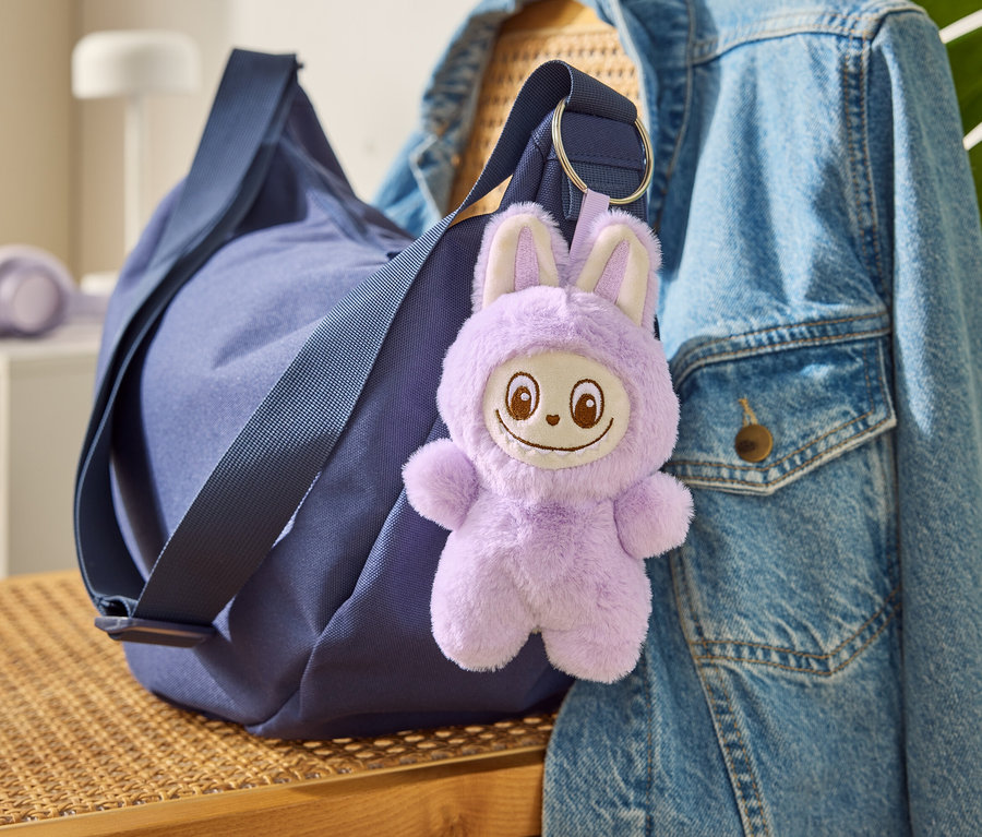 Niebieska torba z brelokiem do kluczy „Tchibobo” wisi na dżinsowej kurtce.